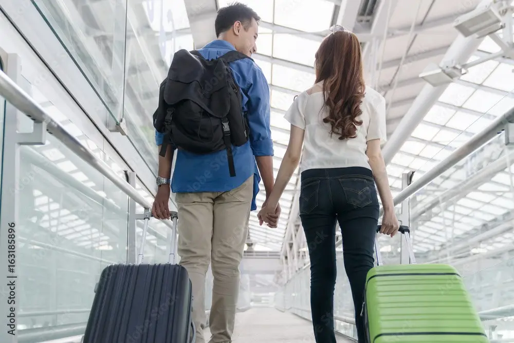 A couple walking with luggage at the airport.